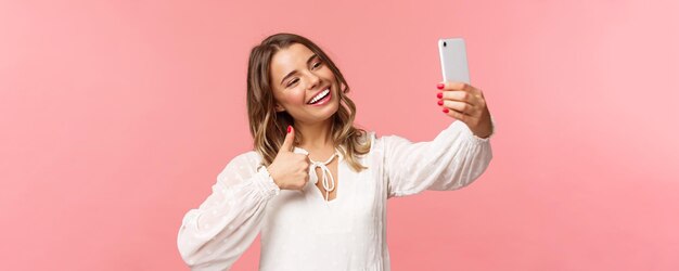 Retrato aproximado de uma bela e estilosa blogueira de beleza grava vídeo em smartphone fazendo selfie mostrando