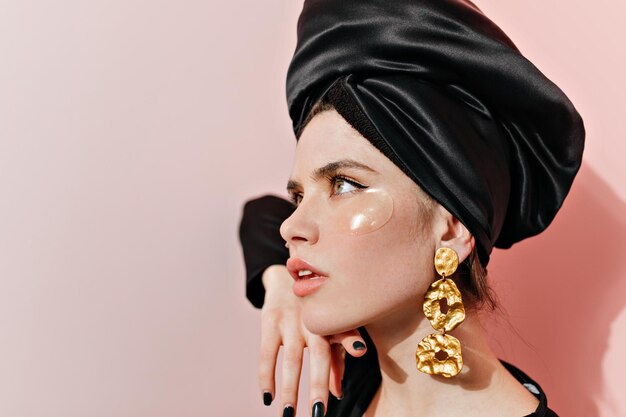 Retrato aproximado de uma jovem linda com grandes brincos dourados usando tapa-olhos Menina europeia pensativa posando em turbante