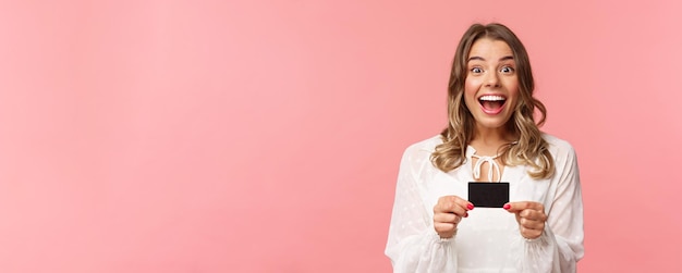 Foto grátis retrato aproximado de uma loira bonita e animada recomenda o banco sorrindo espantado segurando