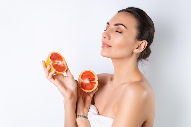 Retrato aproximado de uma mulher em topless com pele perfeita e maquiagem natural lábios nus cheios segurando frutas cítricas frescas vitamina C toranjax9