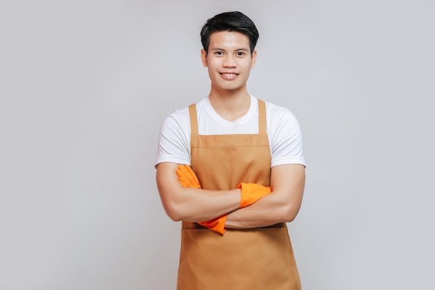 Retrato asiático jovem bonito mand ficar com os braços cruzados, ele usando avental e luvas de borracha, sorrindo e olhando para a câmera, copie o espaço