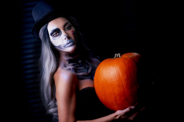 Retrato assustador de mulher com maquiagem gótica de halloween segurando uma abóbora