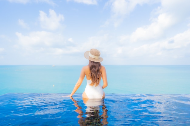 Retrato bela jovem asiática relaxando sorriso lazer ao redor da piscina ao ar livre com o mar oceano em viagens de férias