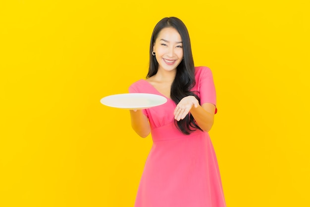 Retrato bela jovem asiática sorrindo com prato vazio na parede amarela