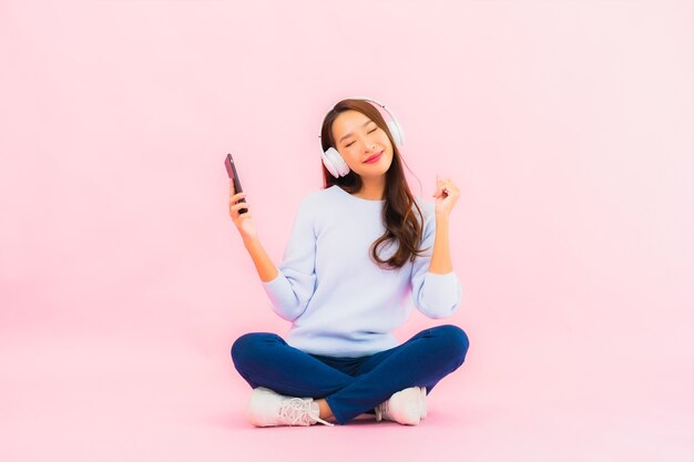 Retrato bela jovem asiática usando telefone celular inteligente com fone de ouvido para ouvir música na parede rosa