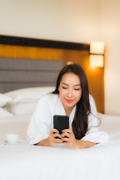 Retrato bela jovem asiática usando telefone celular inteligente na cama, no interior do quarto