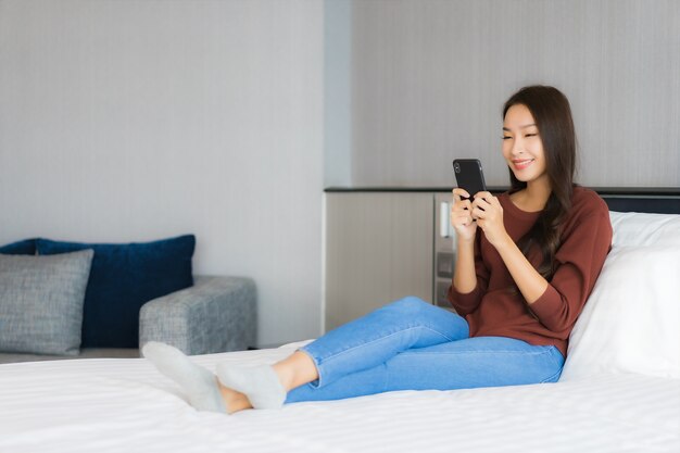 Retrato bela jovem asiática usando telefone celular inteligente na cama, no interior do quarto