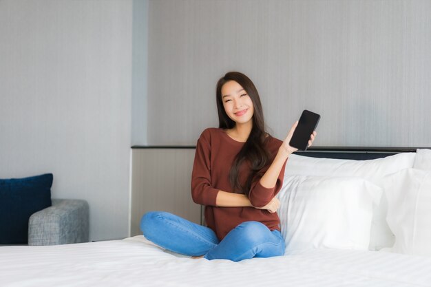 Retrato bela jovem asiática usando telefone celular inteligente na cama, no interior do quarto