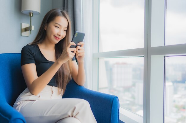Retrato bela jovem asiática usar telefone móvel esperto no sofá na sala de estar