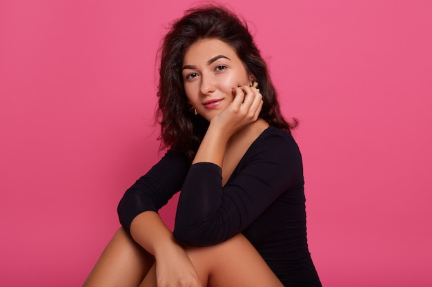 Retrato bela jovem caucasiana, vestindo camisa preta, sentada no chão com as mãos sob o queixo