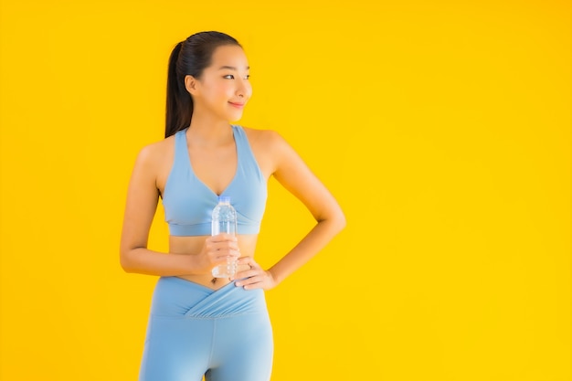 Retrato bela jovem mulher asiática com água de garrafa em amarelo