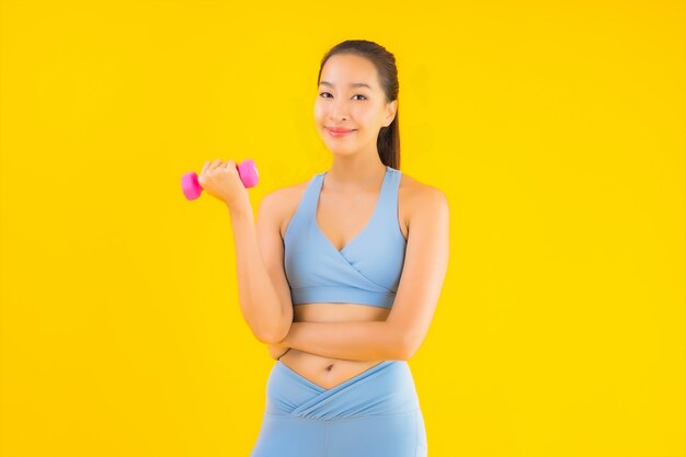 Retrato bela jovem mulher asiática com halteres e sportwear amarelo