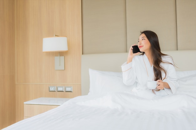 Retrato bela jovem mulher asiática com telefone móvel esperto no quarto