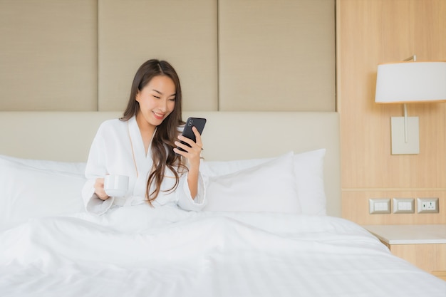 Retrato bela jovem mulher asiática com telefone móvel esperto no quarto