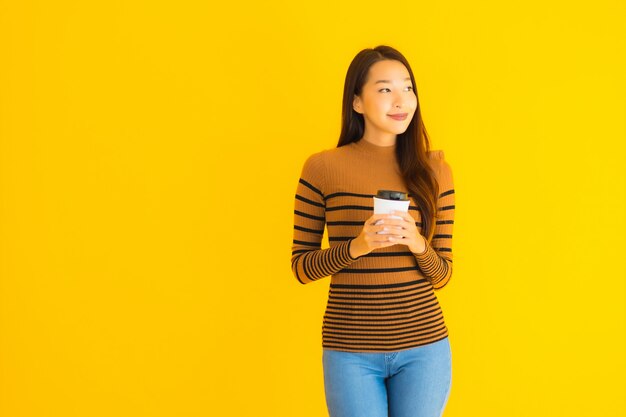 Retrato bela jovem mulher asiática com xícara de café e mochila na mão na parede amarela