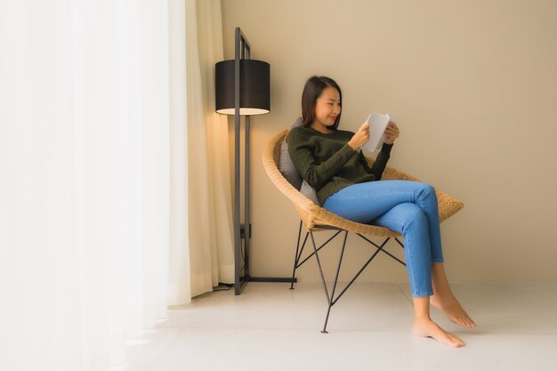 Retrato belas jovens mulheres asiáticas lendo livro e sentado na cadeira do sofá