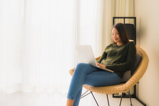 Retrato belas jovens mulheres asiáticas usando computador ou laptop para trabalhar e sentar na cadeira do sofá