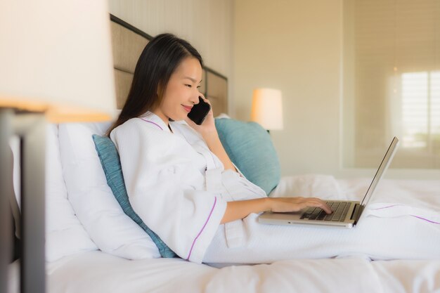 Retrato belas jovens mulheres asiáticas usando laptop ou computador com celular na cama