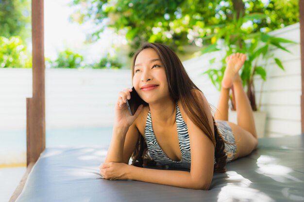 Retrato, bonito, jovem, mulher asian sorri, feliz, relaxe, com, telefone móvel, ao redor, piscina