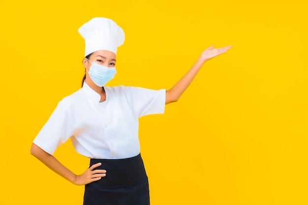 Retrato bonito jovem mulher asiática chef usar máscara para proteger covid19 ou coronavírus em fundo amarelo isolado