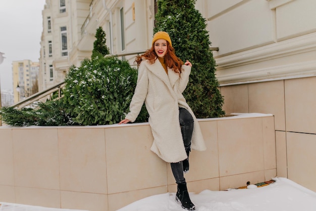 Retrato completo de uma jovem afável de chapéu e casaco Magnífica garota caucasiana com cabelo ruivo se divertindo no inverno