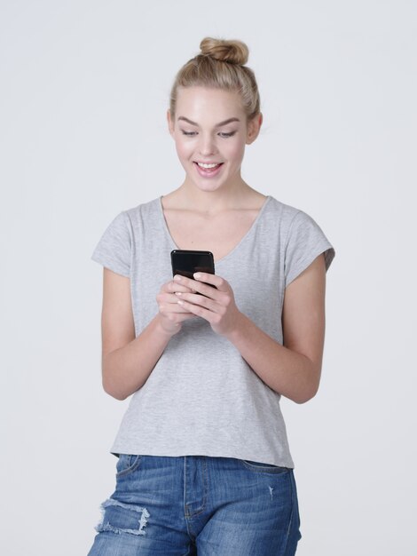 Retrato completo de uma mulher sorridente digitando mensagem de texto no celular - no estúdio