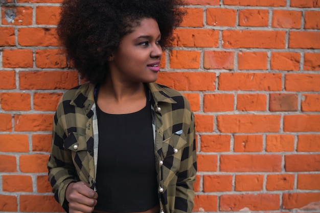 Foto grátis retrato da bela jovem afro-americana do latim, com cabelo encaracolado em pé contra a parede de tijolos.