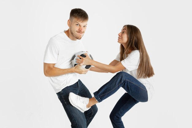 Retrato da bela jovem casal futebol ou fãs de futebol em fundo branco do estúdio. Expressão facial, emoções humanas, publicidade, conceito de esporte. Mulher e homem pulando, gritando, se divertindo.