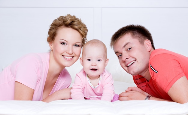 Retrato da bela jovem família feliz deitada na cama em casa