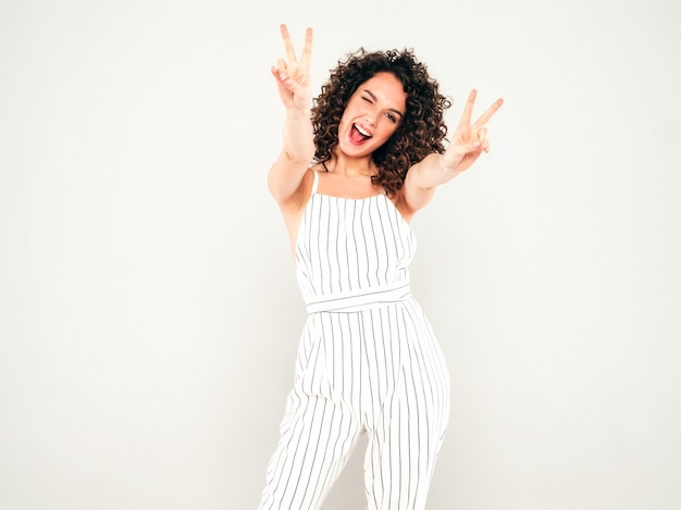 Retrato da bela modelo sorridente com penteado de cachos afro, vestido com roupas de hipster de verão. Na moda, engraçada e positiva mulher mostra sinal de paz