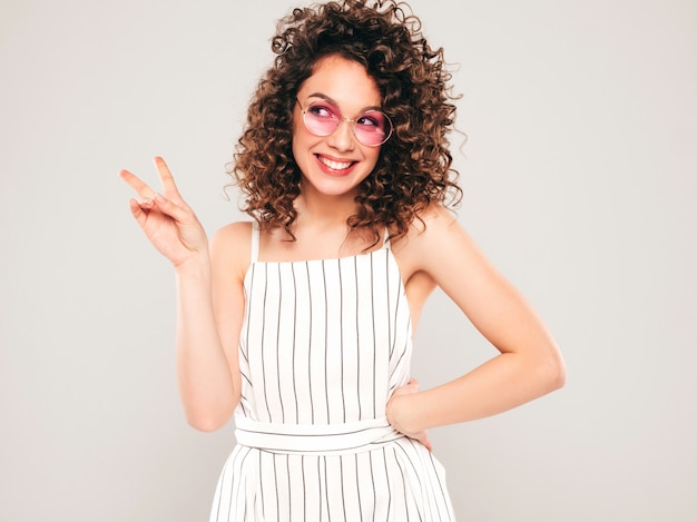 Retrato da bela modelo sorridente com penteado de cachos afro, vestido com roupas de hipster de verão. na moda, engraçada e positiva mulher mostra sinal de paz