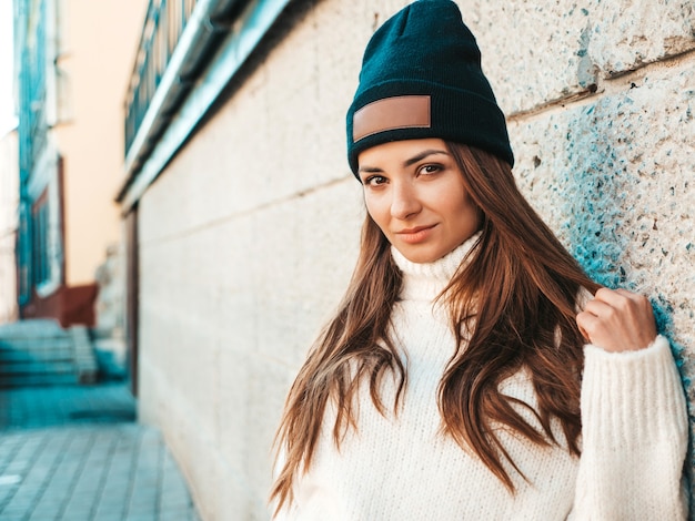 Retrato da bela modelo sorridente. mulher vestida com um gorro e uma camisola branca hippie quente. ela posa na rua