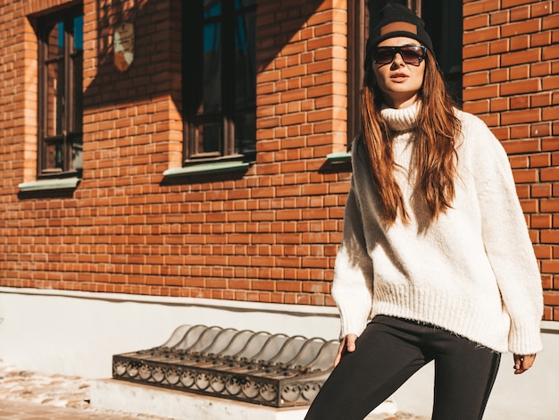 Retrato da bela modelo sorridente. Mulher vestida com um gorro e uma camisola branca hippie quente. Menina na moda posando na rua