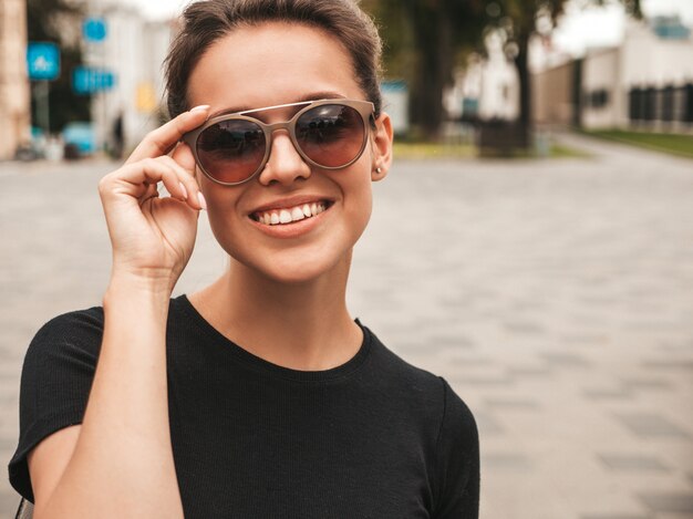 Retrato da bela modelo sorridente, vestido com roupas de verão. Menina na moda posando na rua em óculos de sol. Mulher engraçada e positiva se divertindo