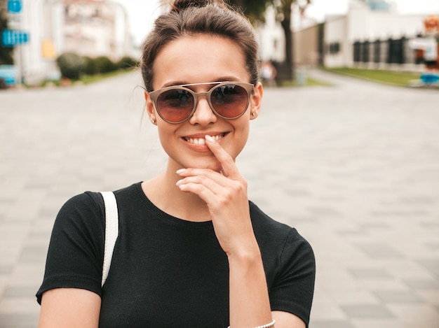 Retrato da bela modelo sorridente, vestido com roupas de verão. Menina na moda posando na rua em óculos de sol. Mulher engraçada e positiva se divertindo