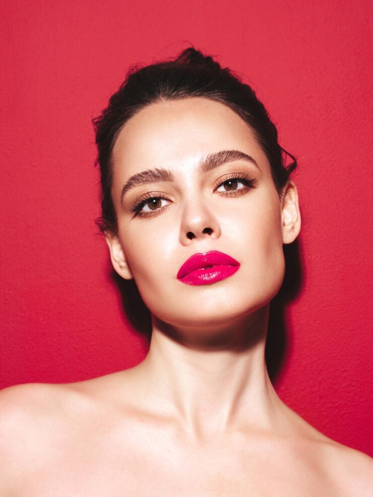 Foto grátis retrato da beleza da moda da jovem morena com maquiagem elegante à noite e pele limpa perfeita modelo sexy com cabelo em um coque posando no estúdio perto da parede vermelha com lábios naturais brilhantes rosa