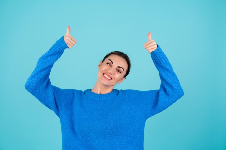 Foto grátis retrato da beleza de uma jovem com um suéter de malha azul e maquiagem natural, sorrindo alegremente e apontando o dedo para um espaço vazio