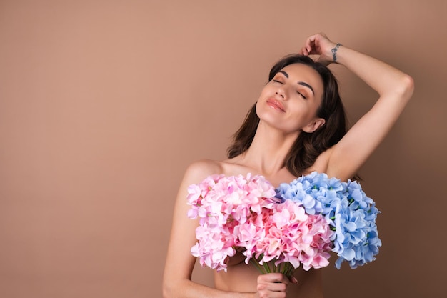 Retrato da beleza de uma mulher em topless com pele perfeita e maquiagem natural em fundo bege segurando buquê de flores coloridas