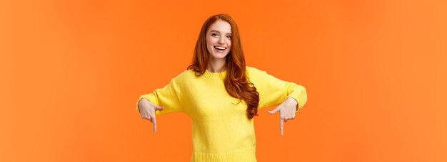 Retrato da cintura para cima, alegre estudante ruiva em suéter amarelo, convidando o evento de check-out recomendado