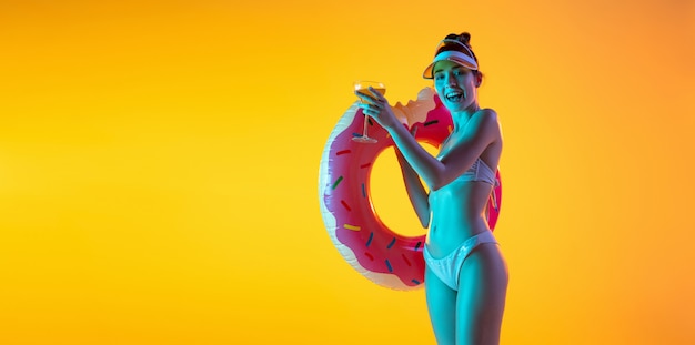 Retrato da moda da garota sedutora em trajes de banho elegante posando em uma parede amarela brilhante. Verão, temporada de praia