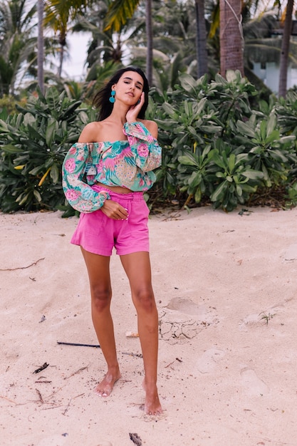 Foto grátis retrato da moda da mulher elegante em top de manga comprida de impressão colorida e shorts rosa na praia, fundo tropical.
