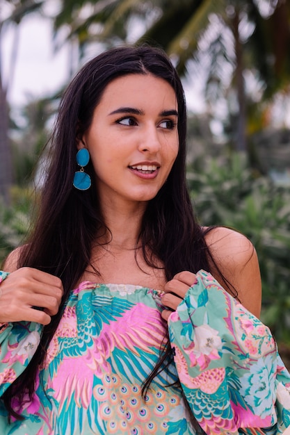 Retrato da moda da mulher elegante em top de manga comprida de impressão colorida e shorts rosa na praia, fundo tropical.