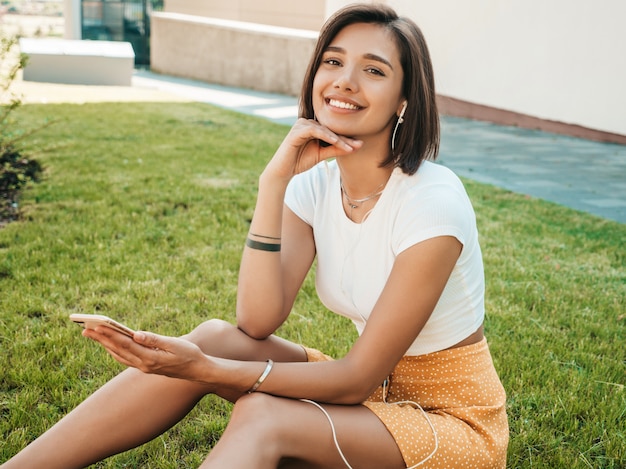 Retrato da moda da mulher jovem hippie elegante. Garota vestindo roupas da moda bonito. Modelo sorridente desfrutar seus fins de semana, sentado no parque. Mulher ouvindo música através de fones de ouvido