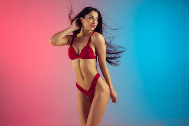 Retrato da moda de jovem em forma e mulher esportiva em um elegante maiô de luxo vermelho na parede gradiente, corpo perfeito pronto para o verão