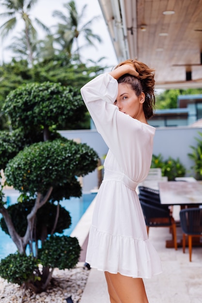 Retrato da moda de uma jovem mulher muito elegante em um vestido branco leve de verão e grandes botas pretas enormes em uma luxuosa villa rica