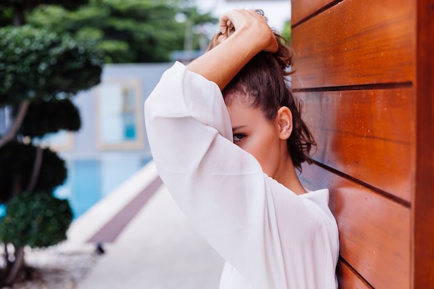 Retrato da moda de uma jovem mulher muito elegante em um vestido branco leve de verão e grandes botas pretas enormes em uma luxuosa villa rica