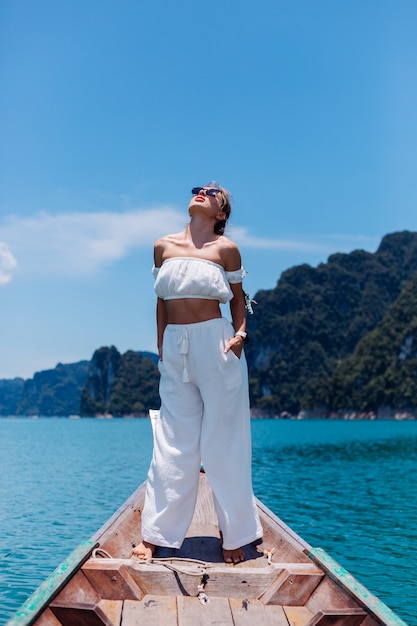 Retrato da moda jovem de blusa branca e calças de férias, na vela de barco de madeira tailandês. conceito de viagens. mulher no parque nacional khao sok.