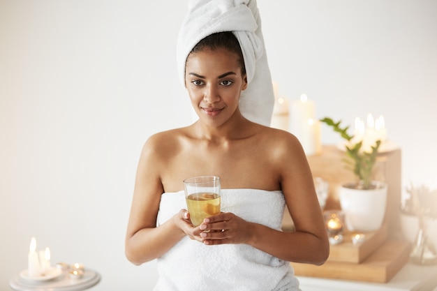 Retrato da mulher africana com a toalha na cabeça que guarda o descanso de sorriso de vidro no spa resort.