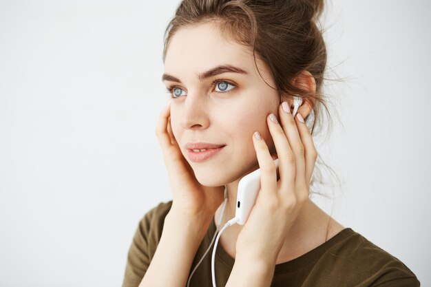 Retrato da música de escuta de sorriso da mulher bonita nova nos fones de ouvido sobre o fundo branco.