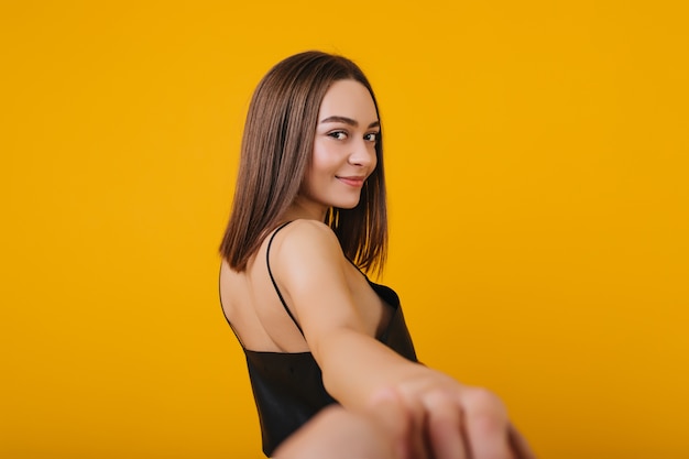 Retrato da parte de trás da linda garota Europeia usa top preto. Mulher linda e jovem com cabelo liso, olhando por cima do ombro com um sorriso.